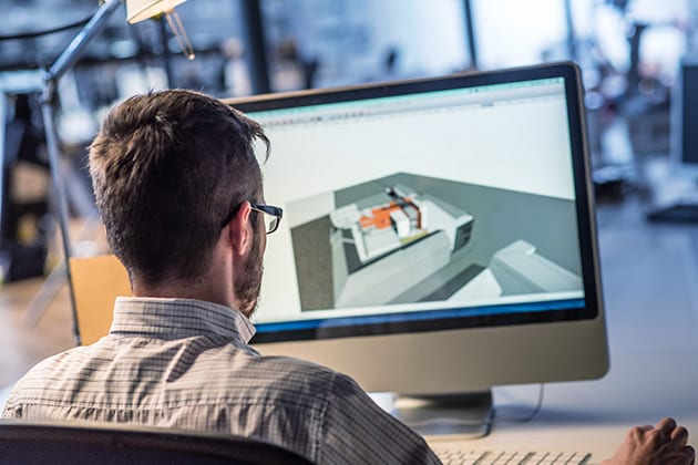 picture of man sitting at desk and looking at computer design of building